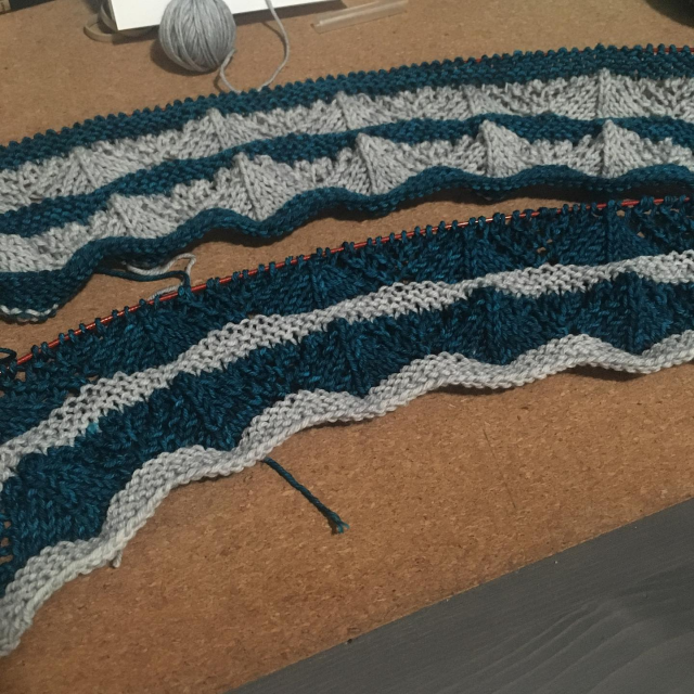 Two knit lace scarves in progress: the top one has blue garter stitch interspersed with gray lace panels, the second has the same pattern with the colors reversed