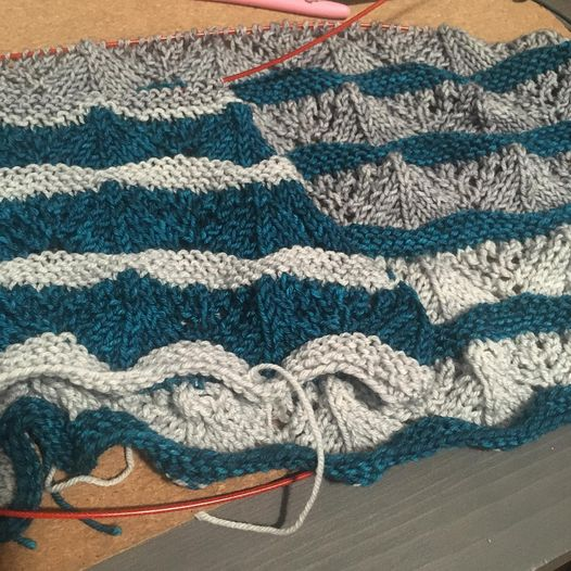 Two knit shawls in progress, stacked on top of each other. They both have lace sections broken up with garter stitch, but the color distribution is reversed on the left and right versions.