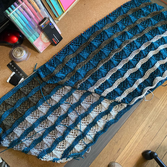 Two knit shawls in progress, each with a garter stitch section and a lace section. The colors placements are reversed on either version.