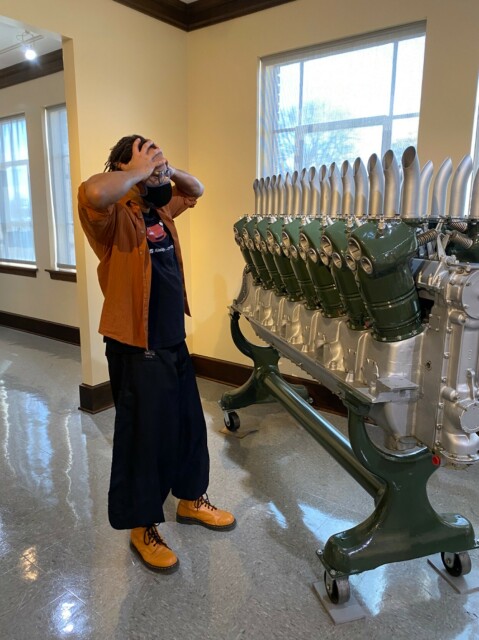 Emmy with their hands on their head, looking shocked, at the scale of the 16 cylinder engine they are standing next to